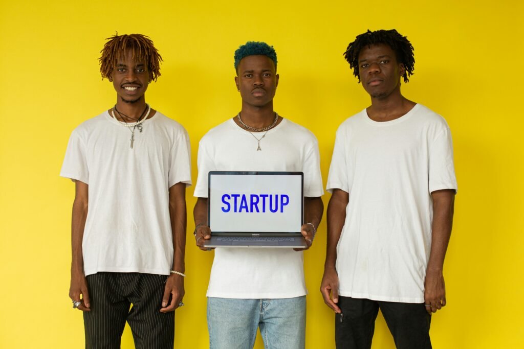 Three men holding a laptop displaying 'STARTUP' against a bold yellow background.